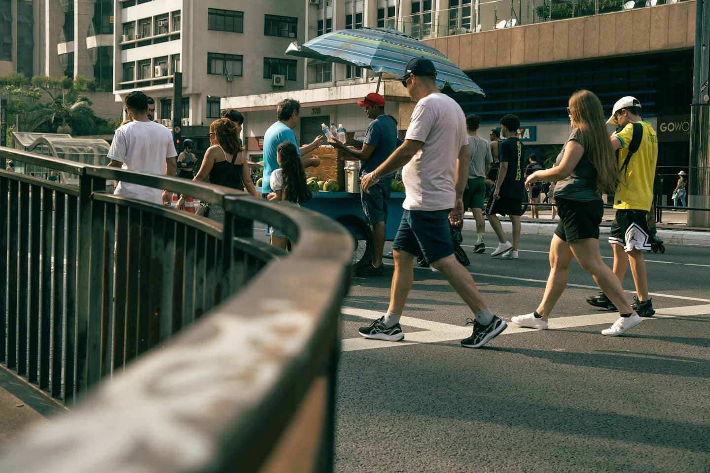 People walk past a street vendor selling coconuts and water.