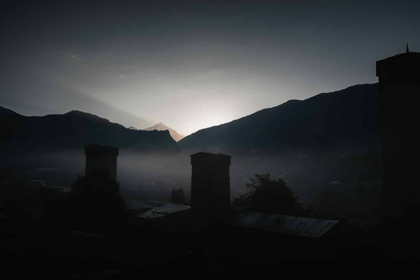 Stone towers and rooftops emerge from mist below jagged mountain peaks.