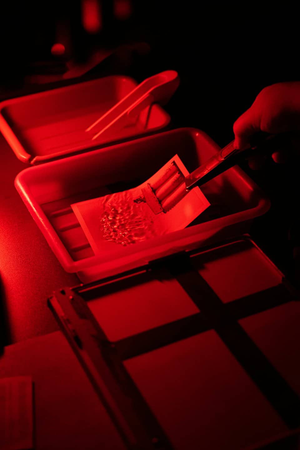 Hand agitates photographic print in darkroom tray.