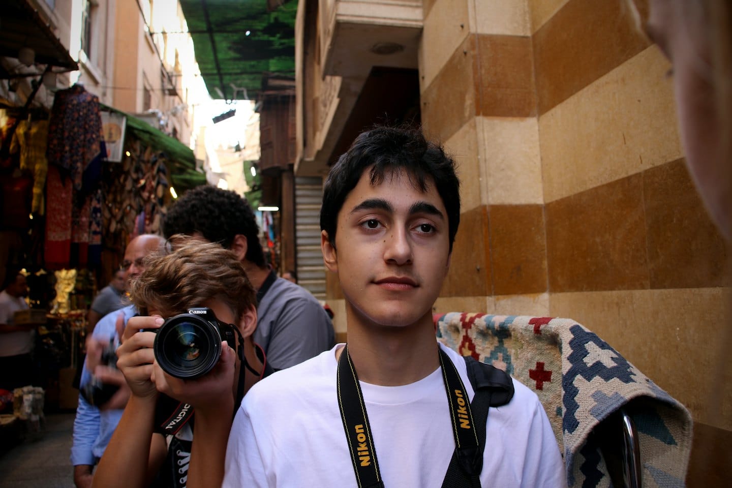 Man with a camera strap stands in a busy market.