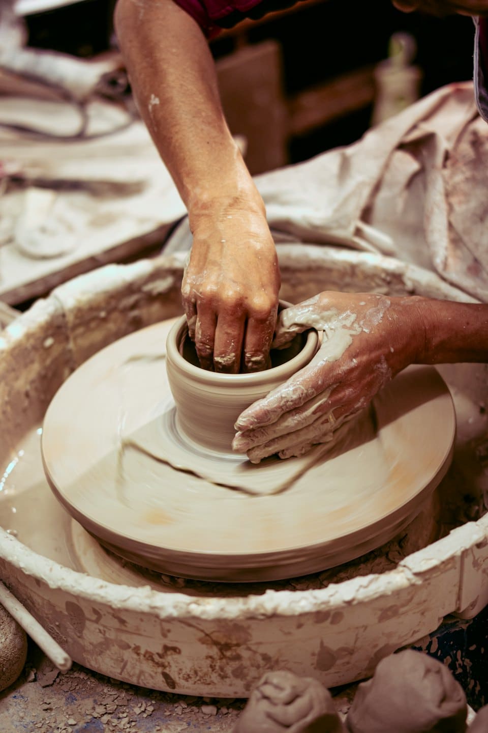 Brown hands covered in clay shape a pot on a wheel.